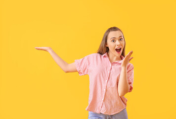 Surprised young woman showing something on color background