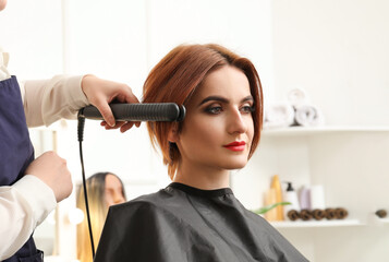 Female hairdresser straightening hair of client in beauty salon