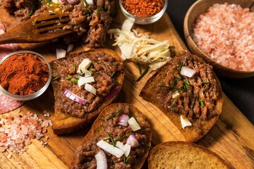 Traditional homemade French steak tartare of raw beef. Steak tartar with chopped onion and herbs on wooden board.