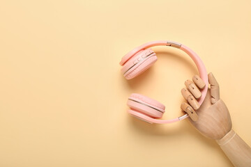 Wooden hand with modern headphones on color background