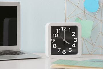 Stylish clock and laptop on table near color wall