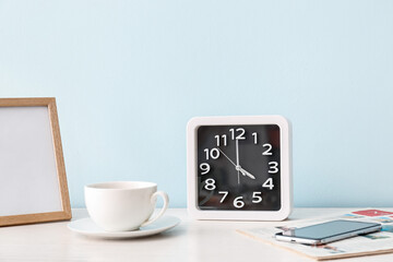 Stylish clock and cup of coffee on table near color wall