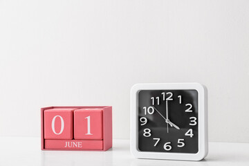 Stylish clock and cube calendar on table near light wall