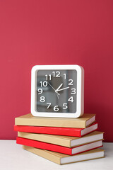 Stylish clock with books on table near color wall