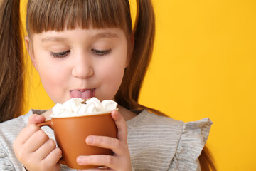 Little girl drinking hot cocoa on color background, closeup