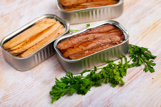 Open can of preserved natural fillet of frigate tuna on wooden table with fresh parsley ..