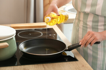Woman pouring sunflower oil onto frying pan in kitchen