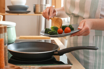 Woman cooking vegetables on frying pan in kitchen