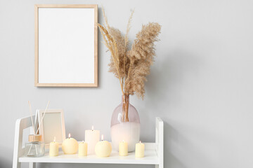 Shelf with burning candles and vase near light wall