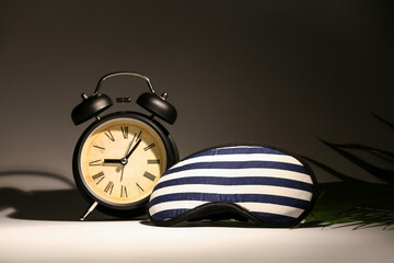 Stylish clock with sleeping mask on dark background