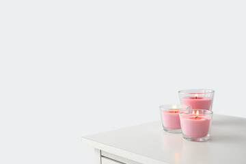 Burning candles on shelf near light wall