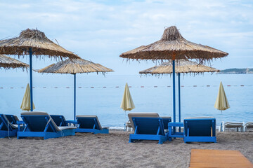 Empty white sun loungers without people under umbrellason the pebble beach by the sea.