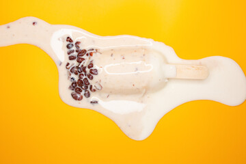 top view half melted milkshake flavor popsicle with red beans on a yellow background