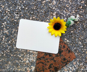A white card with a plastic sunflower in the top right corner is placed on a stone table.