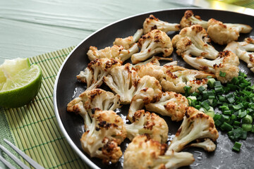 Frying pan with tasty fried cauliflower and green onion on table, closeup