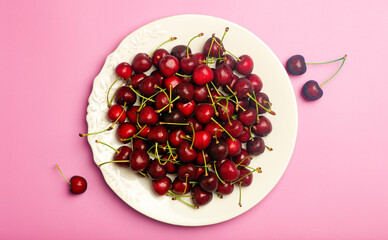 Cherry background. Red juicy sweet cherry on a white plate on a light pink background. Summer fresh juicy berries and food concept