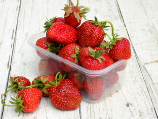 Strawberries in a transparent container on a wooden table.