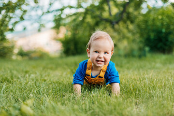 A baby boy lies on the grass in the garden and laughs