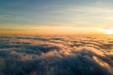 Fototapeta na wymiar Aerial view of vibrant yellow sunrise over white dense clouds with blue sky overhead.