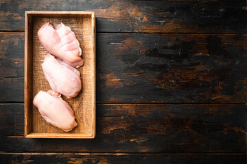 Chicken breast fillets, in wooden box, on old dark  wooden table background, top view flat lay, with copy space for text