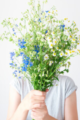 The woman holds the bouquet with both hands and covers her face. Minimal composition with wild and meadow flowers close-up.