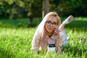 sexy blonde woman talking on the mobile phone and lying on meadow