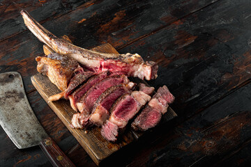 Traditional barbecue dry aged wagyu tomahawk steak sliced, on wooden serving board, on old dark  wooden table background, with copy space for text