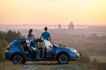 Happy couple standing near their car at sunset. Young man and woman enjoying time together...