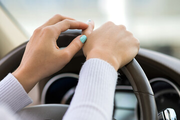 Close up view of woman holding steering wheel driving a car on city street on sunny day.