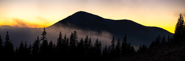 Beautiful mountain panorama of landscape with hazy peaks and foggy wooded valley at sunset.