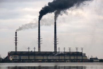 Obraz premium Coal power plant high pipes with black smoke moving upwards polluting atmosphere with reflections of it in lake water.