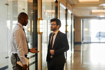 Side view portrait of two businessmen chatting in office building hall, copy space