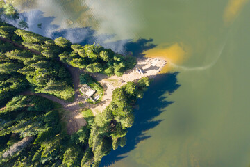 Top down aerial view of big lake with clear blue water between high mountain hills covered with dense evergreen forest.