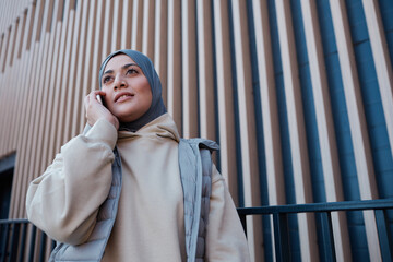 Graphic waist up portrait of modern Middle-Eastern woman speaking by smartphone in city, copy space