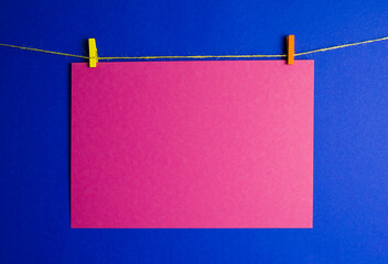 a red sheet of paper is suspended on a rope on a blue background. cardboard is held on a yellow and...