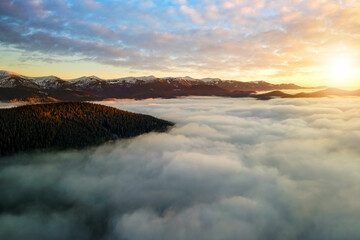 Aerial view of vibrant sunrise over white dense clouds with distant dark mountains on horizon.