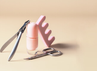 Modern nail care still life.  Manicure scissors, cuticle nipper cutter , toe separator and nail polish on beige background.
