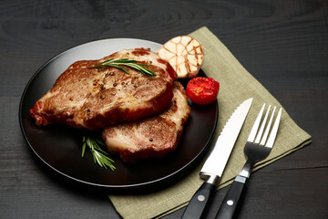 Grilled roated beef steaks on black ceramic plate