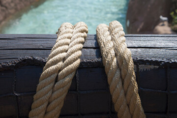 Close-up of a nautical mooring rope with a knotted end tied around a cleat on a wooden pier nautical