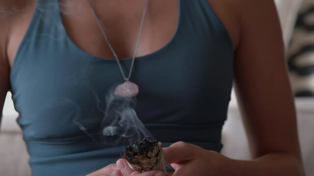 Woman sitting on the carpet meditating and burning sage wearing crystal necklace