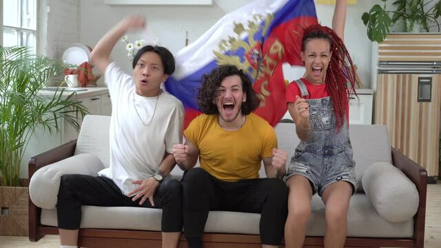 Happy Russian fans watch sports on TV at home. Fans with the flag of Russia