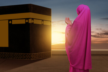 Rear view of Asian Muslim woman in a veil standing and praying with Kaaba view
