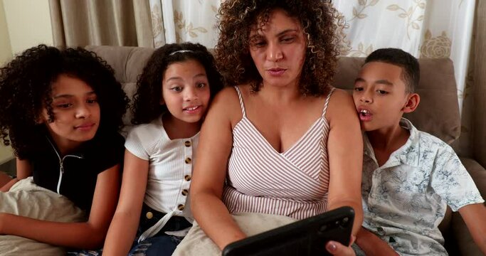 Brazilian mother and children staring at cellphone screen together at home sofa surprised reaction