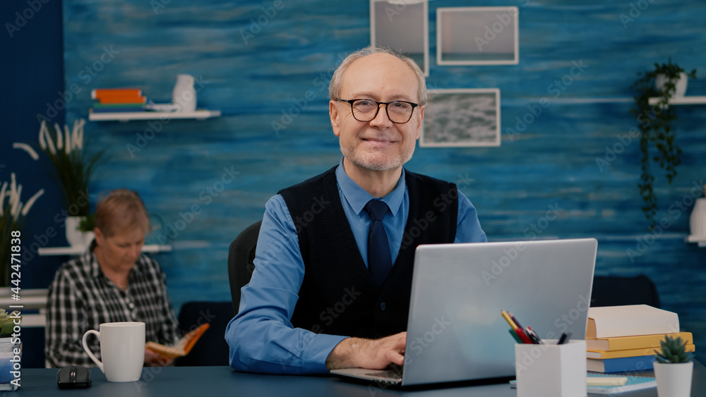 Aufkleber retired manager sitting at desk in front of camera smiling after typing at laptop working from home 
