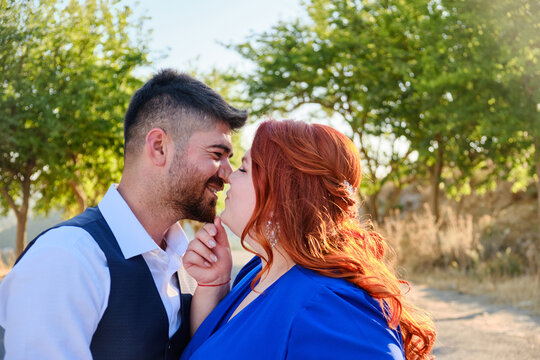 Caucasian plus size red headed woman kisses her turkish beloved man. Mixed race couple hugs and kisses on a walk. Middle eastern man and caucasian woman marriage or engagement