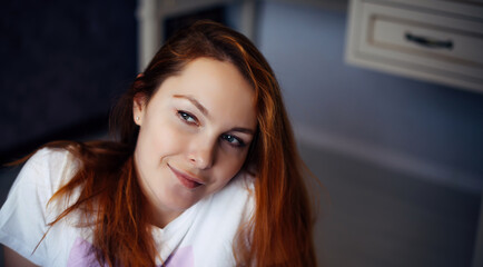 Portrait of young red-haired woman with perfect smooth skin. Face of beautiful girl, close-up. Female model in white t-shirt looks at camera and smiles.