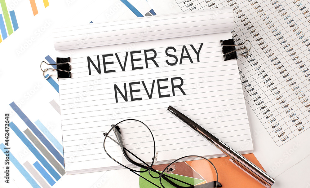 Poster notebook with text never say never on table with charts,pen and glasses.