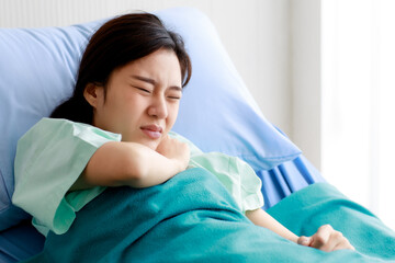 Asian beautiful young female patient lying on bed in hospital and touching her chest with pain while being heart disease. Medical Treatment and Health Concept.