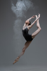 Skilled ballerina dancing leaping against gray background