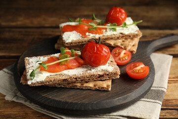 Fototapeta na wymiar Fresh rye crispbreads with salmon, cream cheese and tomatoes on wooden table, closeup